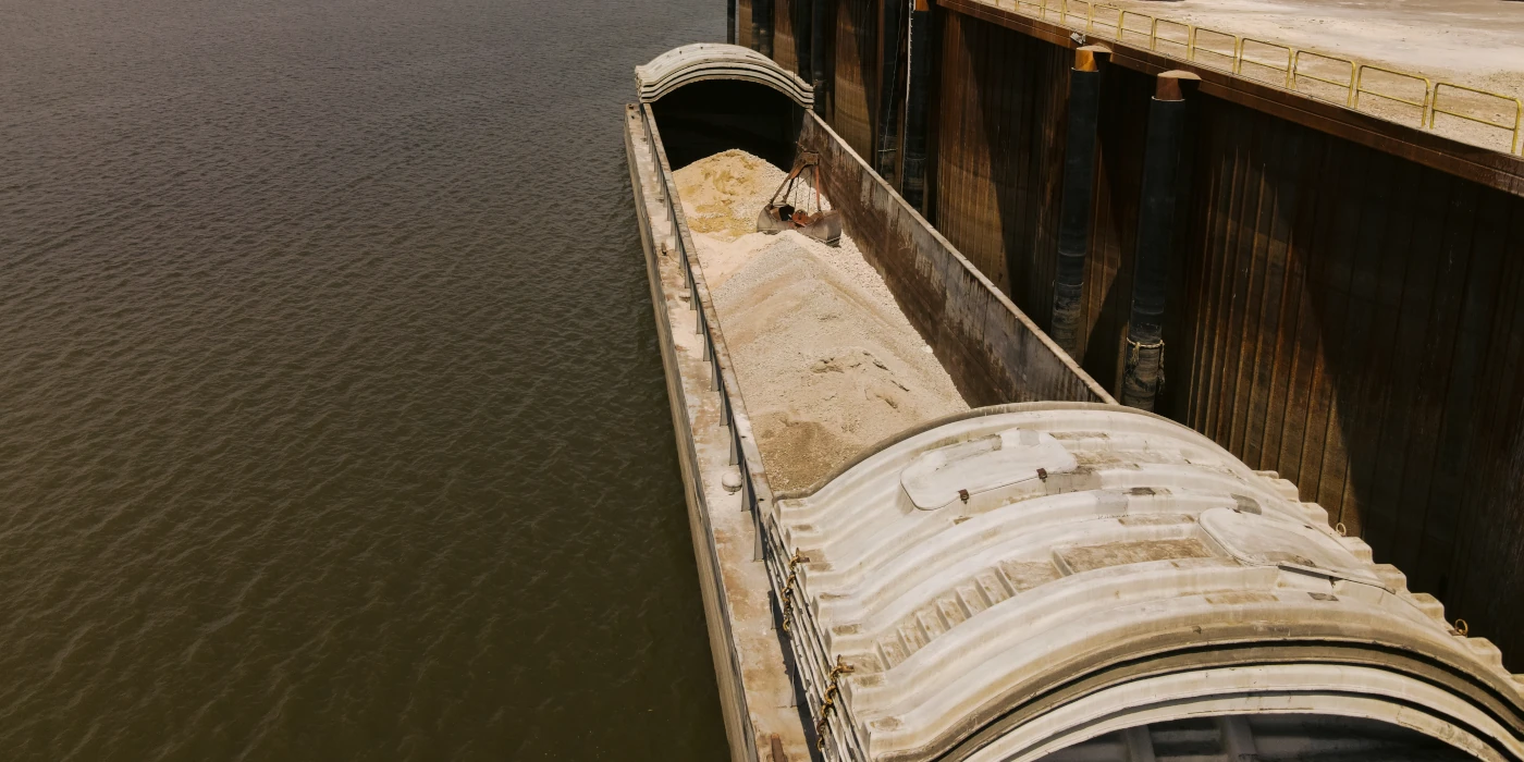 A barge loaded with sand is docked at a waterfront industrial facility.