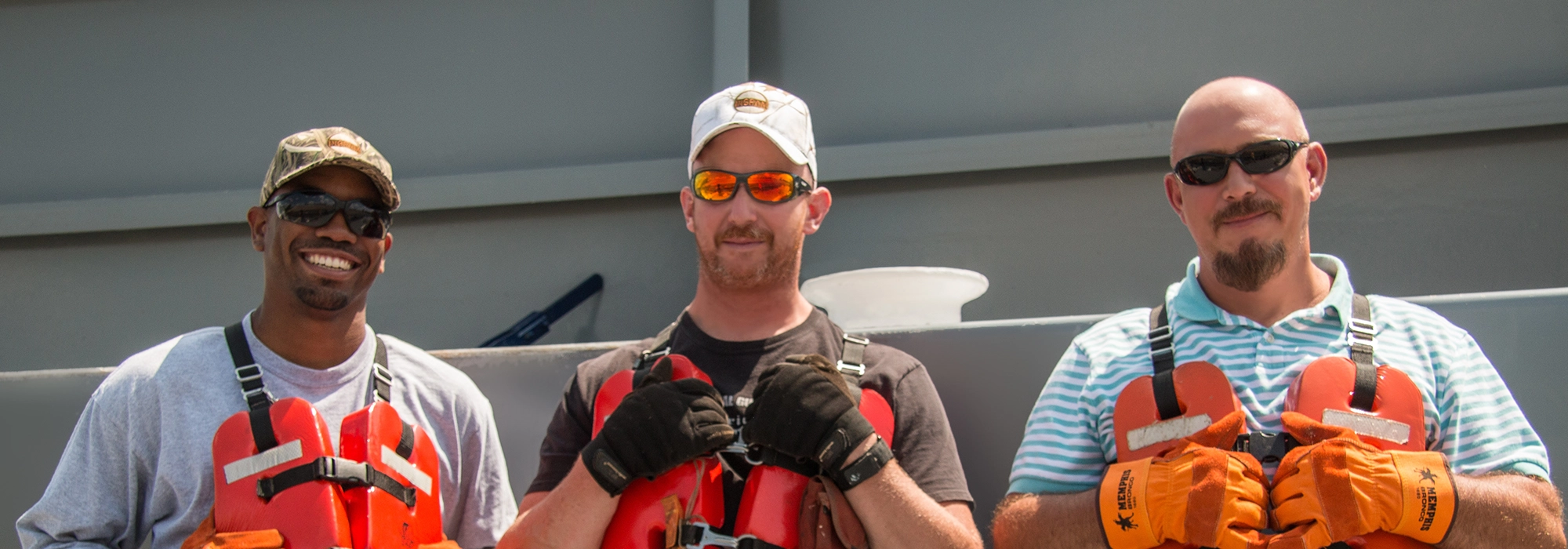 Three men wearing life vests and gloves stand side by side outdoors, facing the camera.